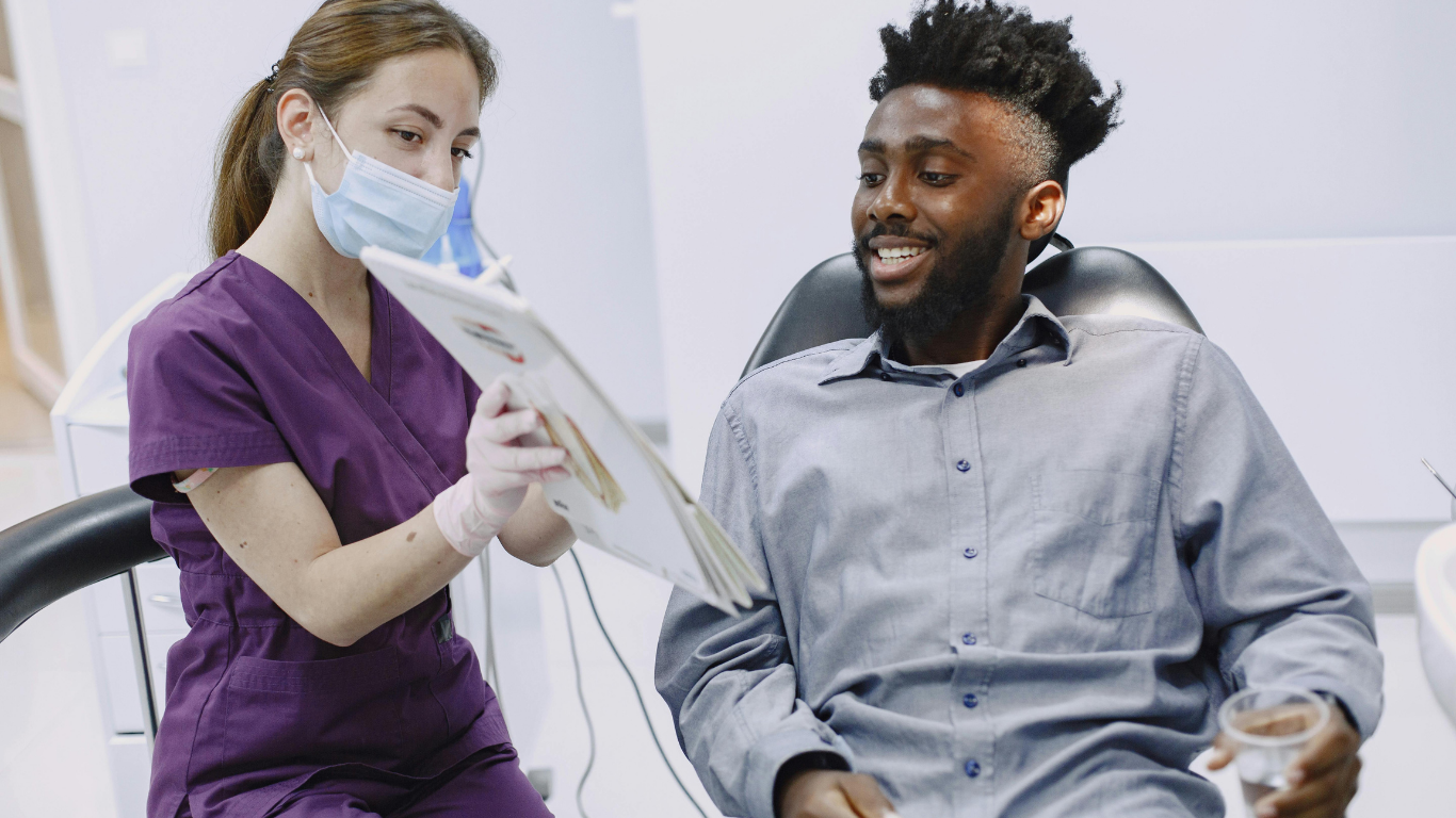 Gloved dentist demonstrating toothbrush use on a dental model against a blue background