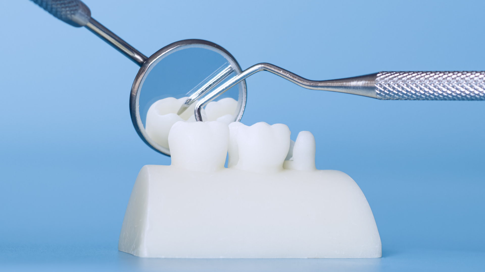 Dental mirror reflecting a white tooth model with an implant on a blue background
