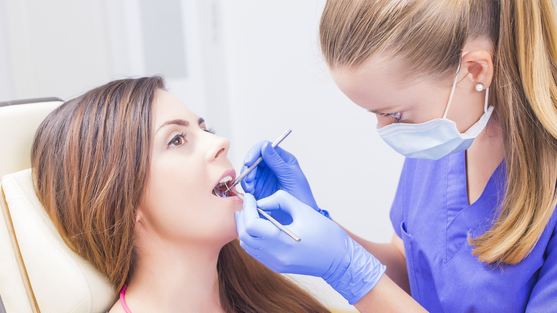 Dentist examining patient in dental chair, holding tools. Smiling patient, medical setting, logo visible.