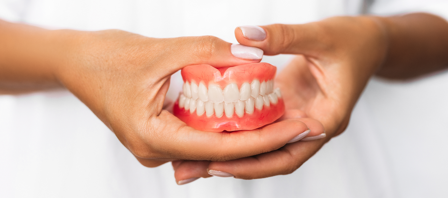A woman is holding a denture in her hands.