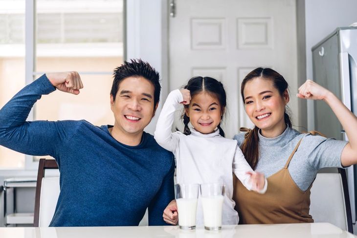 A family is sitting at a table with glasses of milk and flexing their muscles.
