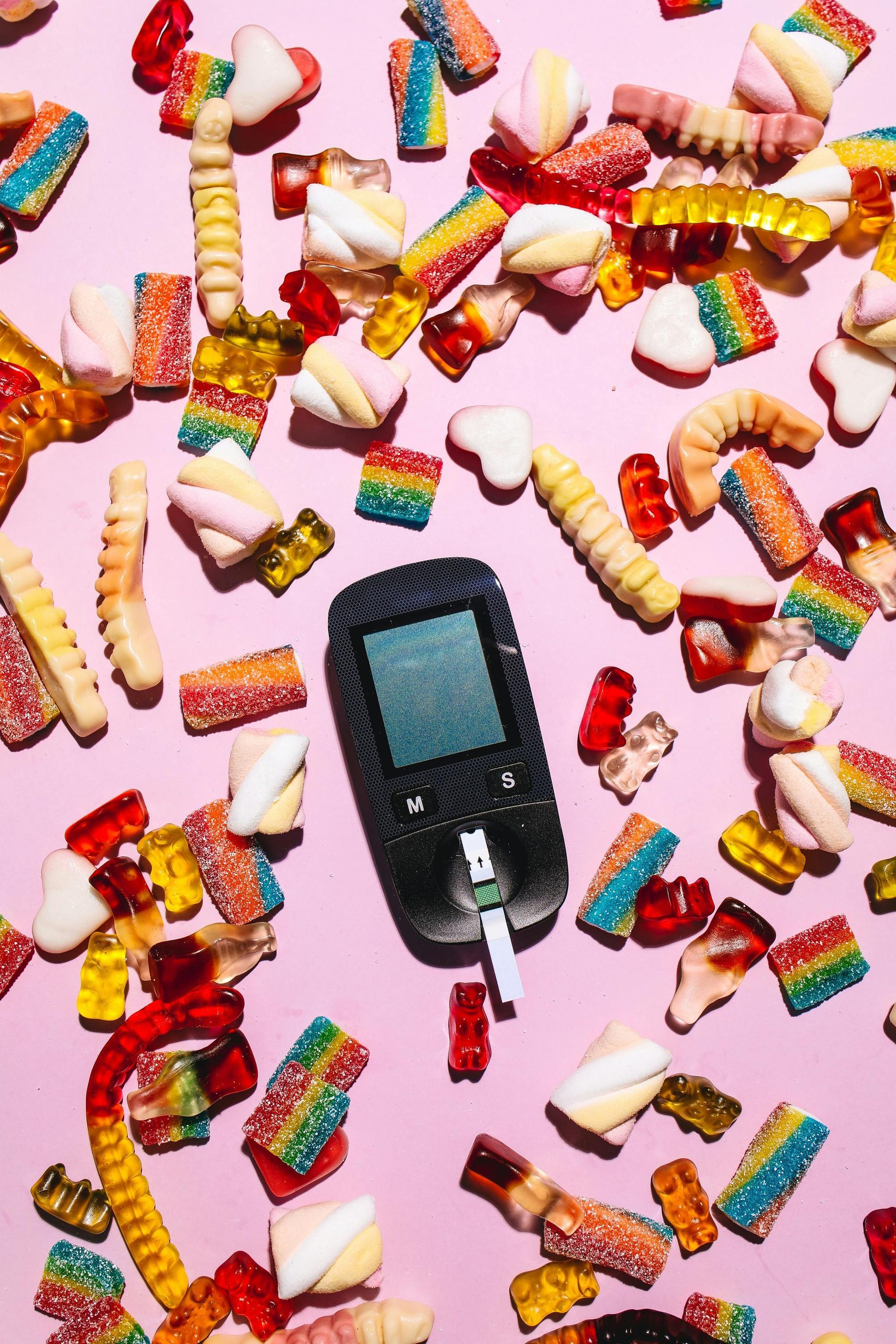 Um monitor de diabetes está cercado por doces em um fundo rosa.