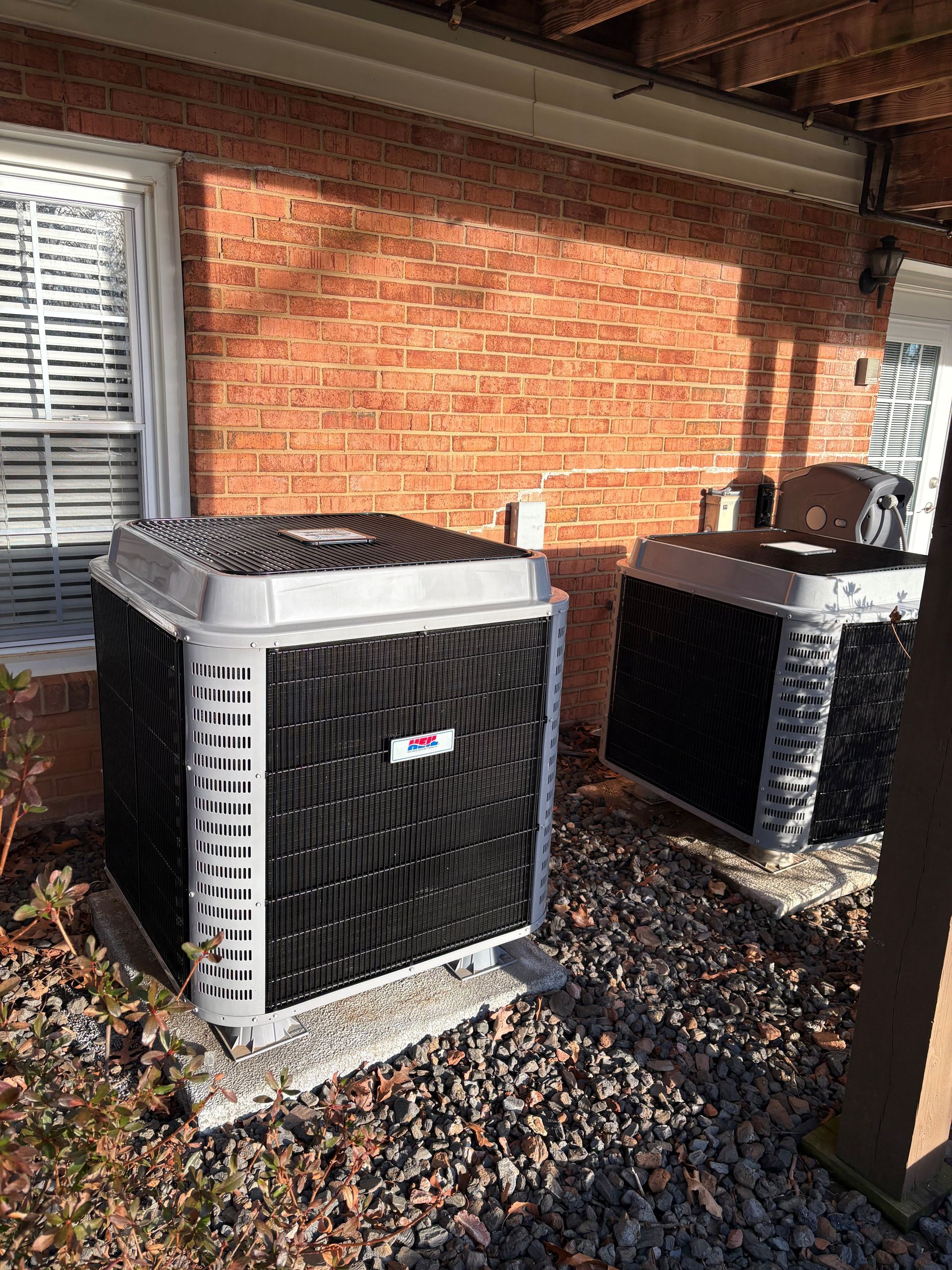 An air conditioning unit mounted on a white building exterior, with a cloudy sky in the background.