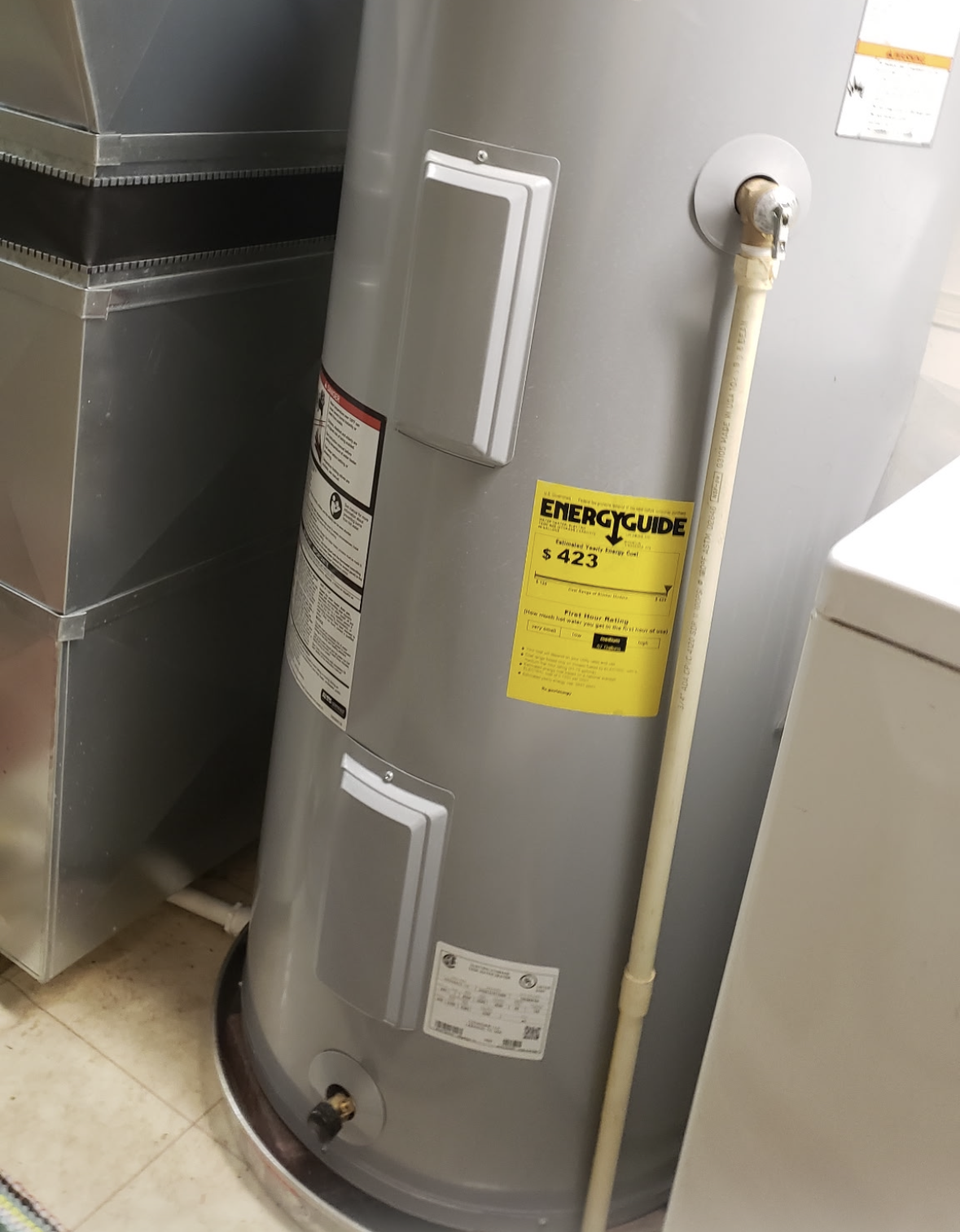 Woman in striped shirt checks phone near a water heater in a utility room. Woman in striped shirt checks phone near a water heater in a utility room.