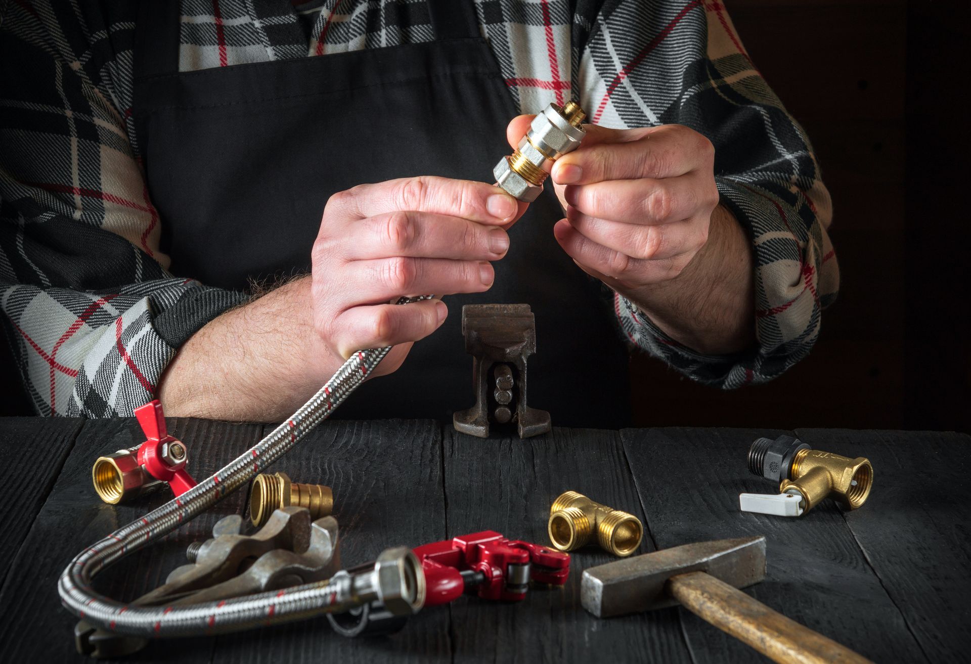 Plumber assembling plumbing parts on a dark wooden table, wearing a plaid shirt and black apron. Plumber assembling plumbing parts on a dark wooden table, wearing a plaid shirt and black apron.