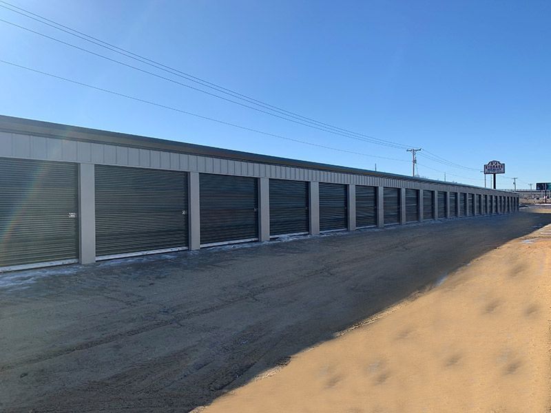 Row of storage unit doors along a gravel lot under a clear blue sky