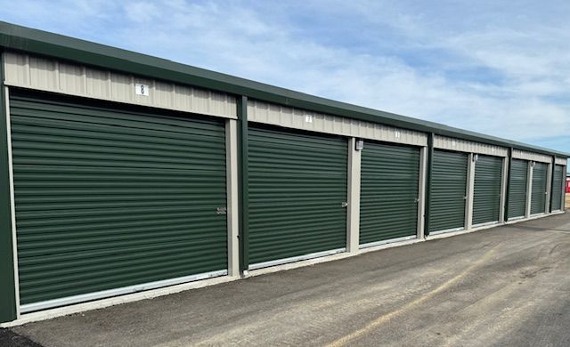 Row of green storage unit doors under a long white roof along a paved lot