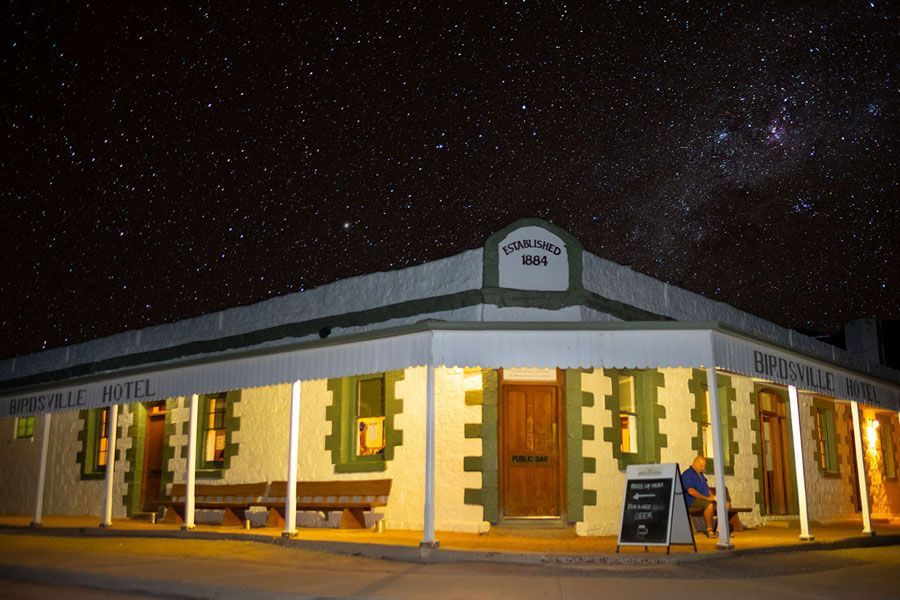 Hotel exterior under a starry night sky. Green trim, wooden door, person seated outside.