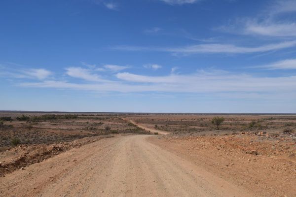 Dirt road leading through arid, brown landscape under a blue sky with wispy clouds.