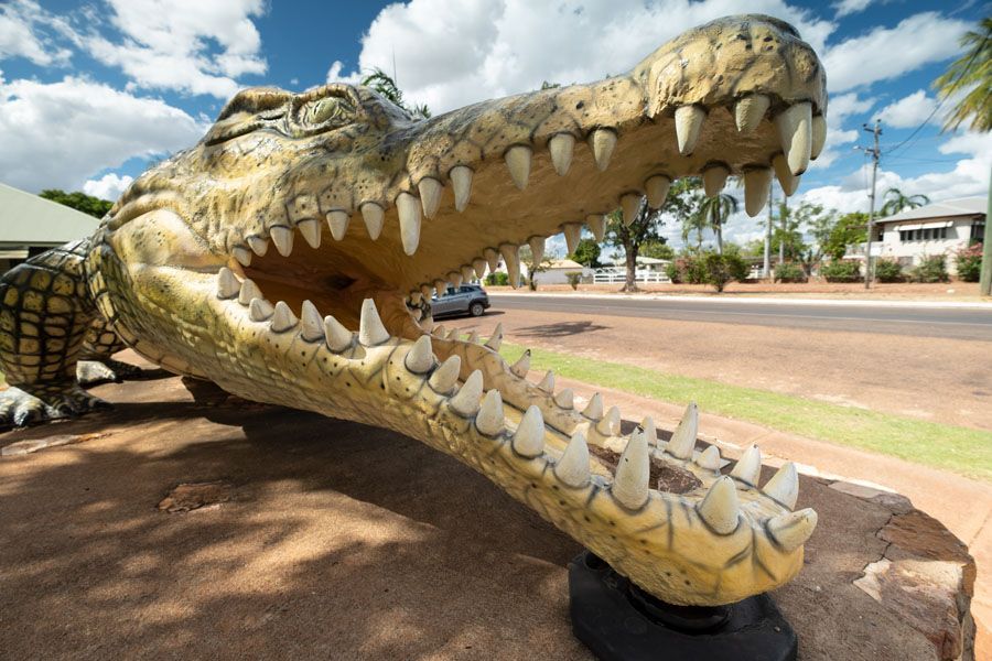 Giant crocodile statue with open mouth on a sidewalk in front of a street.