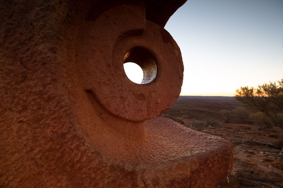 Stone sculpture with a circular opening against a desert landscape at sunset.