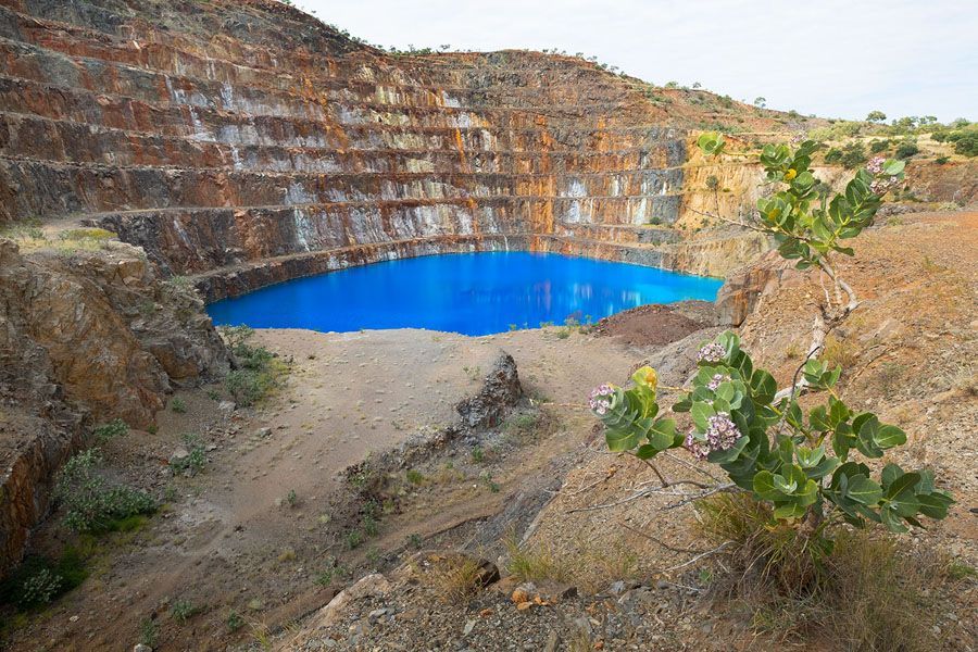 Open-pit mine filled with vibrant blue water, surrounded by brown, layered rock walls.