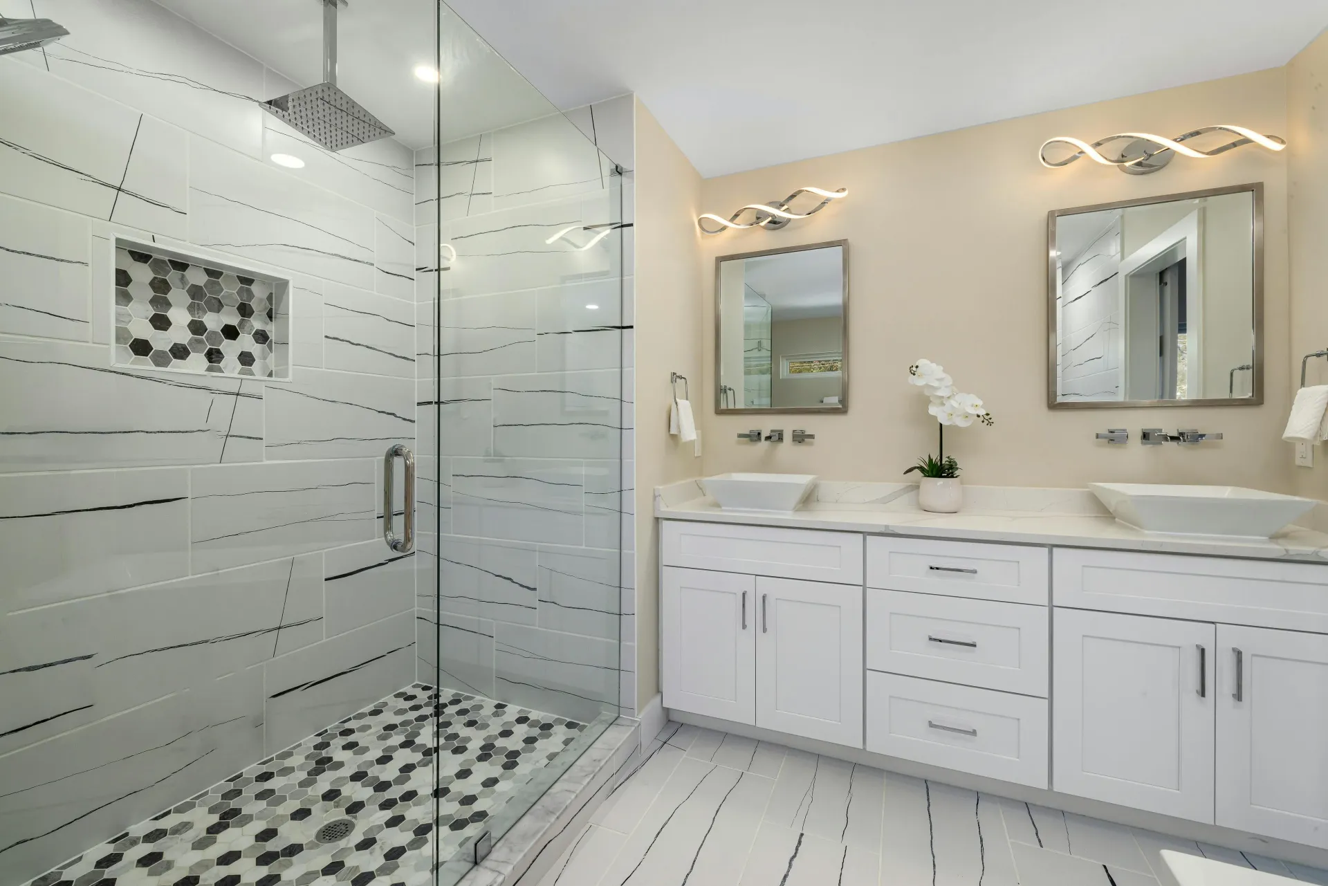 Modern bathroom with a glass shower, double vanity, white cabinets, and light fixtures.