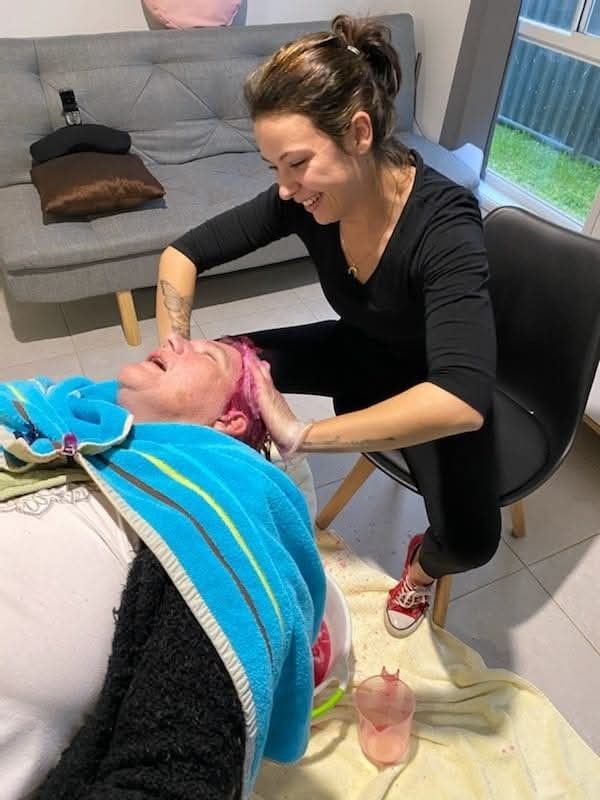 Woman giving scalp massage to another woman, indoors. One has pink hair.