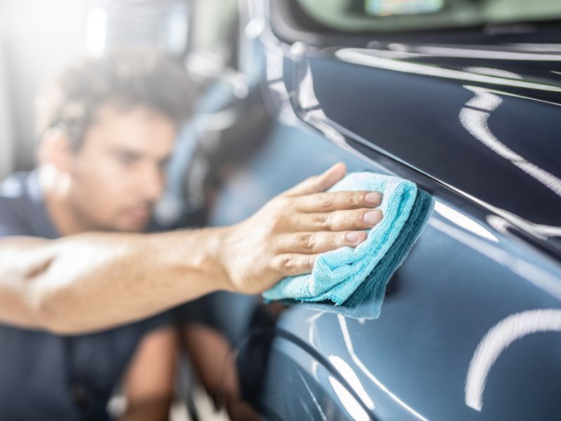 Hand polishing a dark blue car with a turquoise cloth in a garage