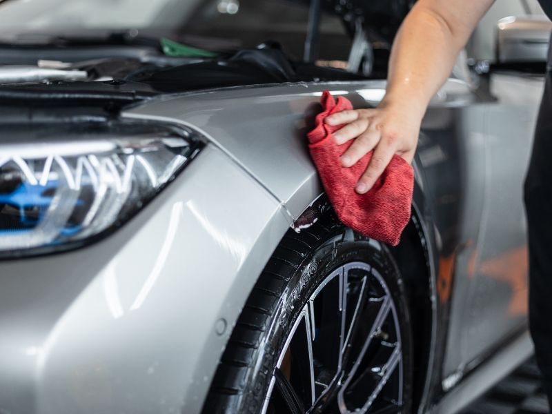 Person wiping a silver car&rsquo;s fender with a red cloth in a garage