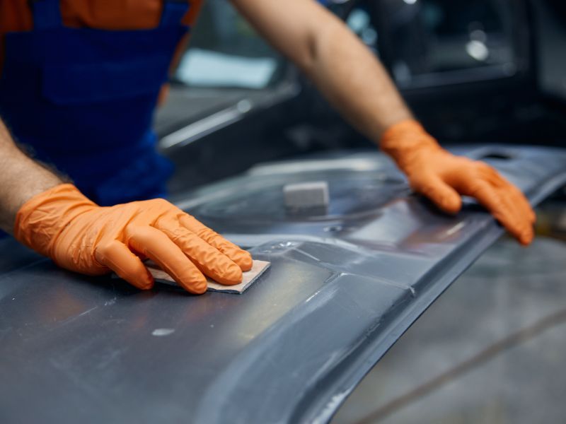 Gloved hands cleaning a car surface with a cloth in a workshop