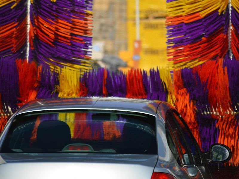 Car covered in colorful red, purple, and orange cloth strips, seen from the front