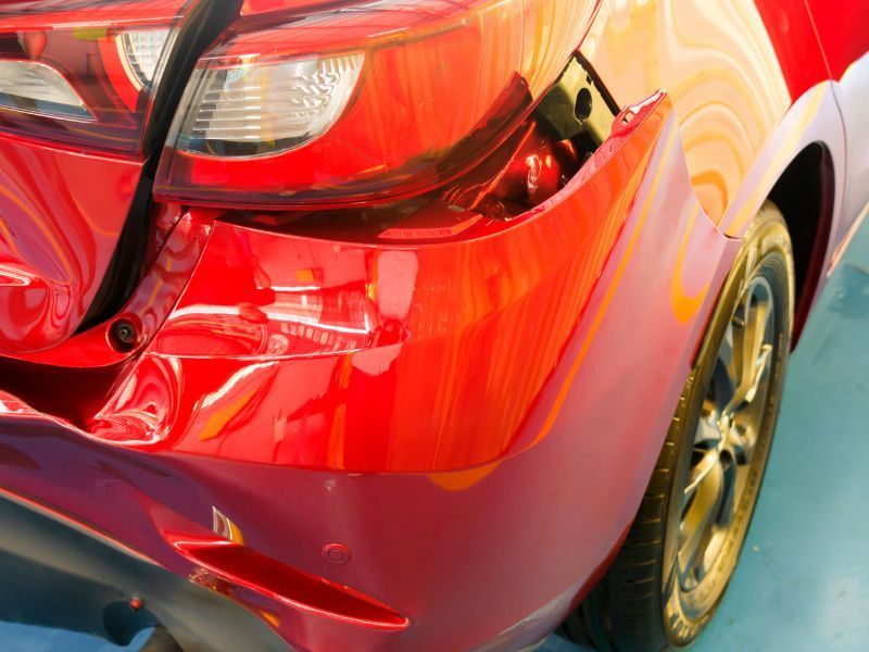 Close-up of a red car&rsquo;s rear quarter panel with a visible dent and scratched paint