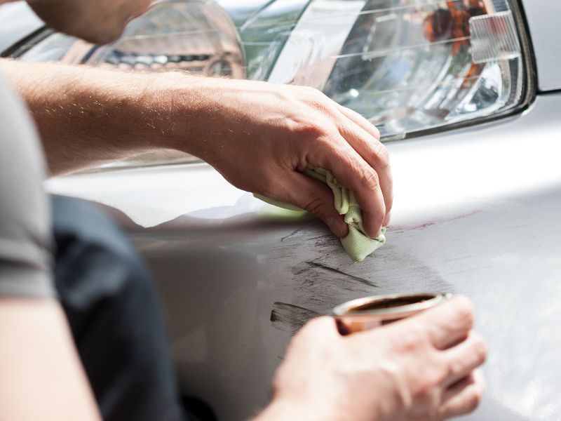 Hands sanding a white car door panel with a sponge, preparing it for paint
