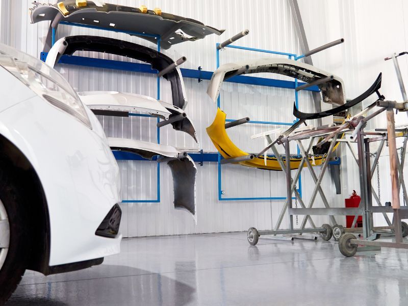 Car assembly line with a white car body and hanging painted parts in a bright factory workshop