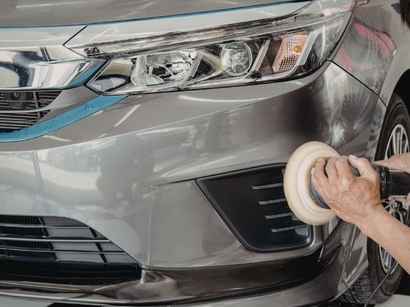Hand polishing the front bumper of a gray car with a buffing pad
