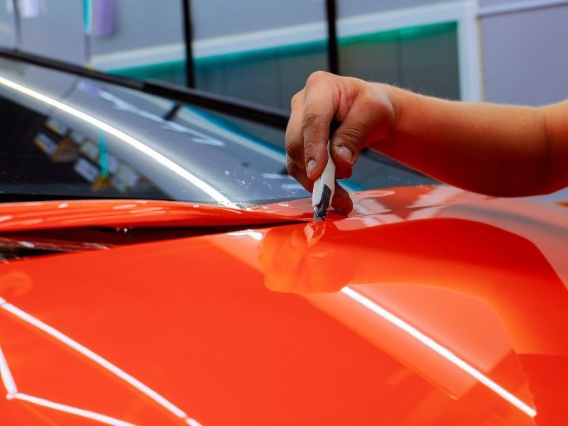 Hand polishing a shiny red car hood with a cloth