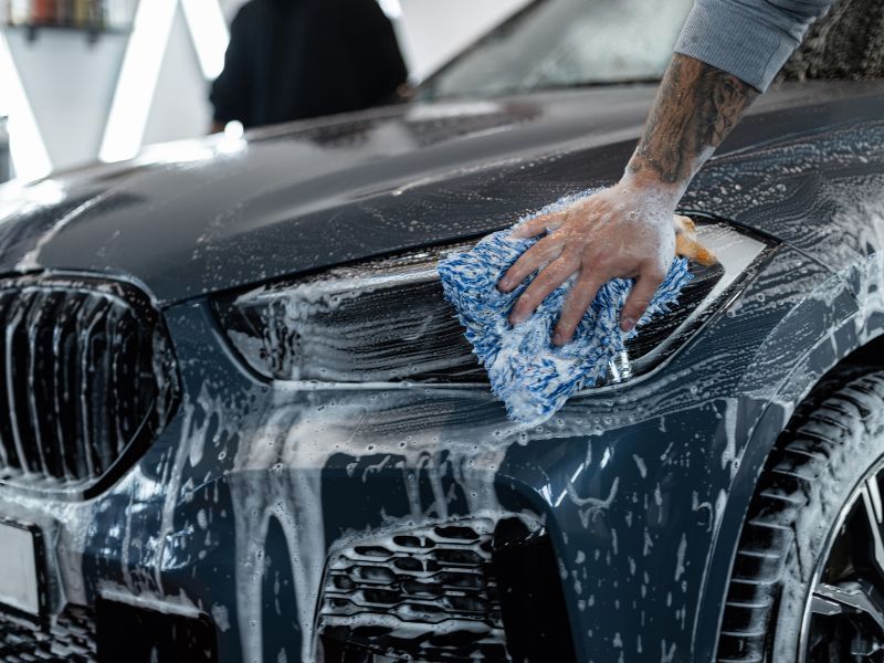 Hand washing a black BMW car with soap and a blue sponge