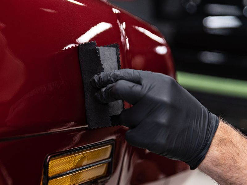Gloved hand polishing a red car near a rear light with a buffing pad
