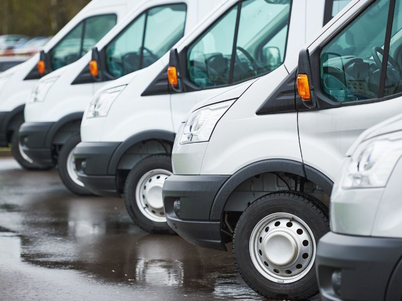 Row of white delivery vans parked in a wet lot, side view