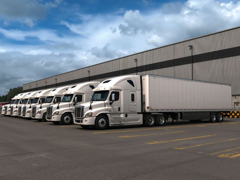 White semi-trucks lined up outside a warehouse loading dock under a cloudy sky