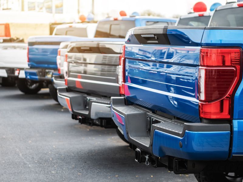 Row of parked pickup trucks in blue, white, and gray, viewed from the rear in a lot