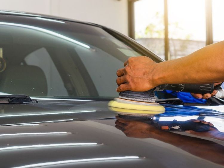 Hand polishing a black car hood with a buffer in a garage