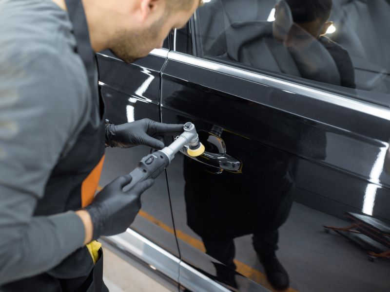 Technician polishing a black car door with a buffer in a garage