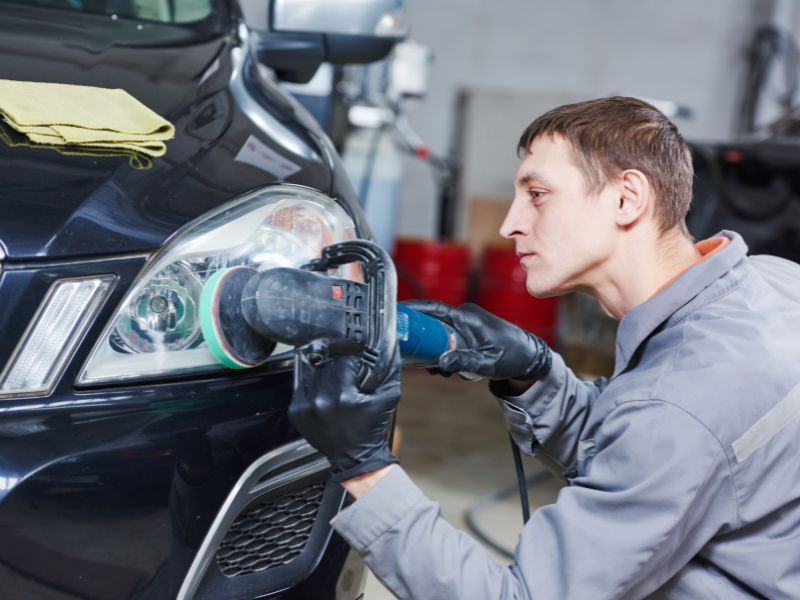 Mechanic polishing a black car headlight in an auto shop
