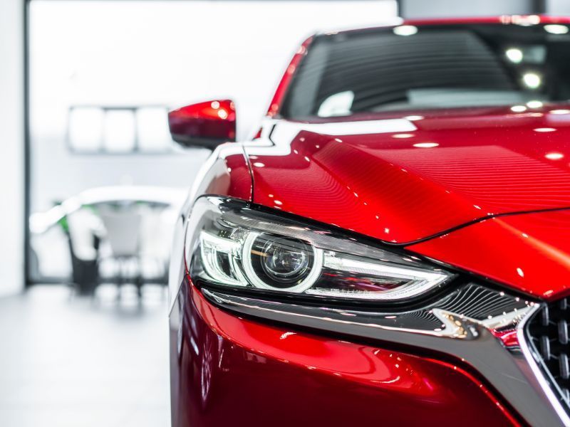 Close-up of a red sports car&rsquo;s front headlight in a bright showroom