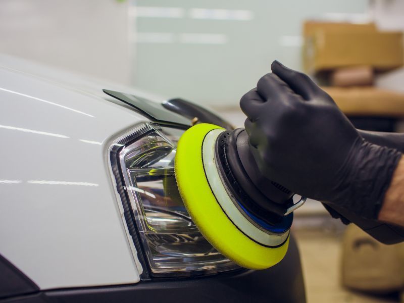 Gloved hand polishing a car headlight with a yellow buffer pad