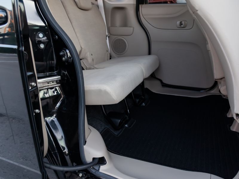 Car interior with folded rear seat and open door, showing gray upholstery and black floor mat