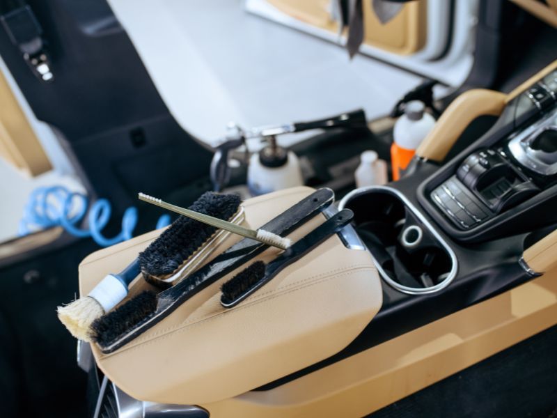 Car center console with black-and-beige trim, gear shifter, cupholders, and a wire brush resting on the armrest