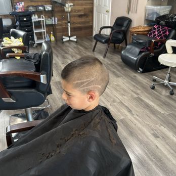 A young boy getting a haircut in a barbershop. He has a design shaved into his hair.