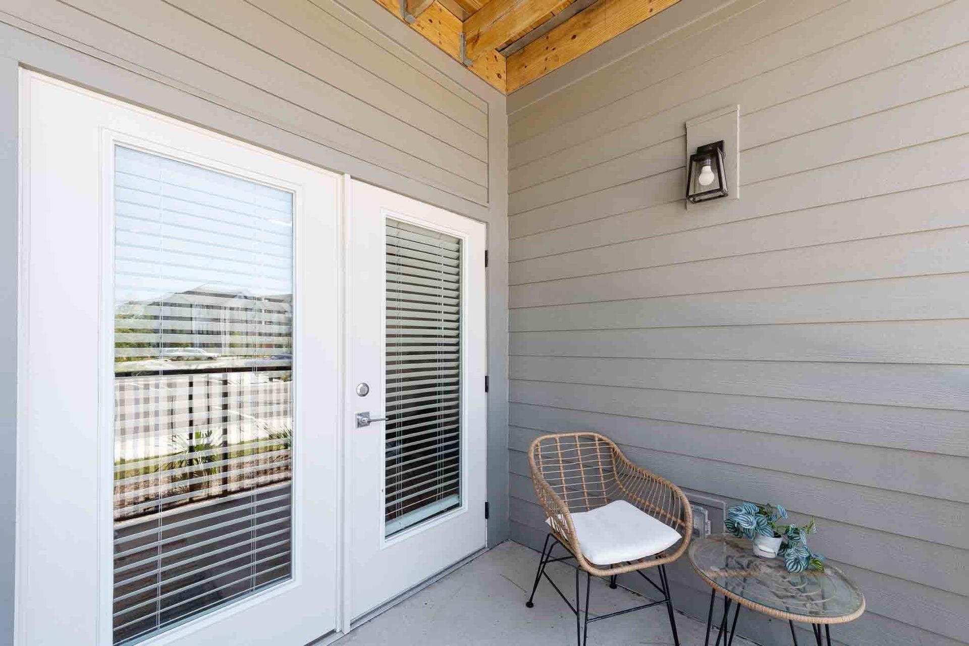Balcony with French doors, wicker chair, small table, and outdoor light on gray siding.