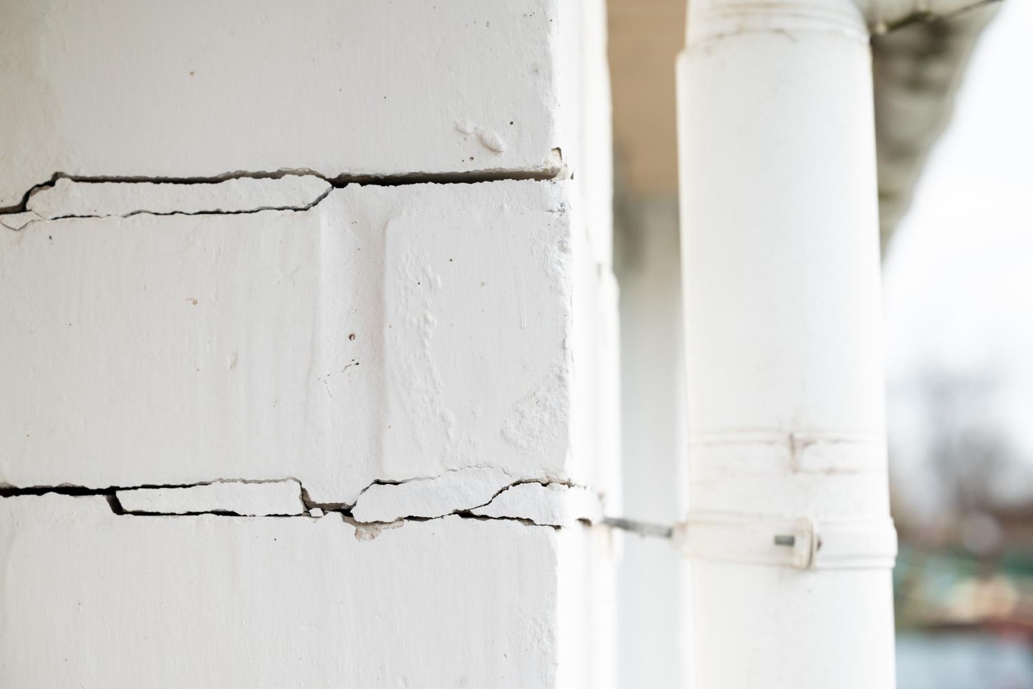 Cracked white exterior wall beside a white downspout and pipe