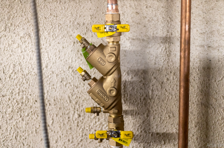 Brass plumbing valve assembly with yellow handles on copper pipes against a concrete wall
