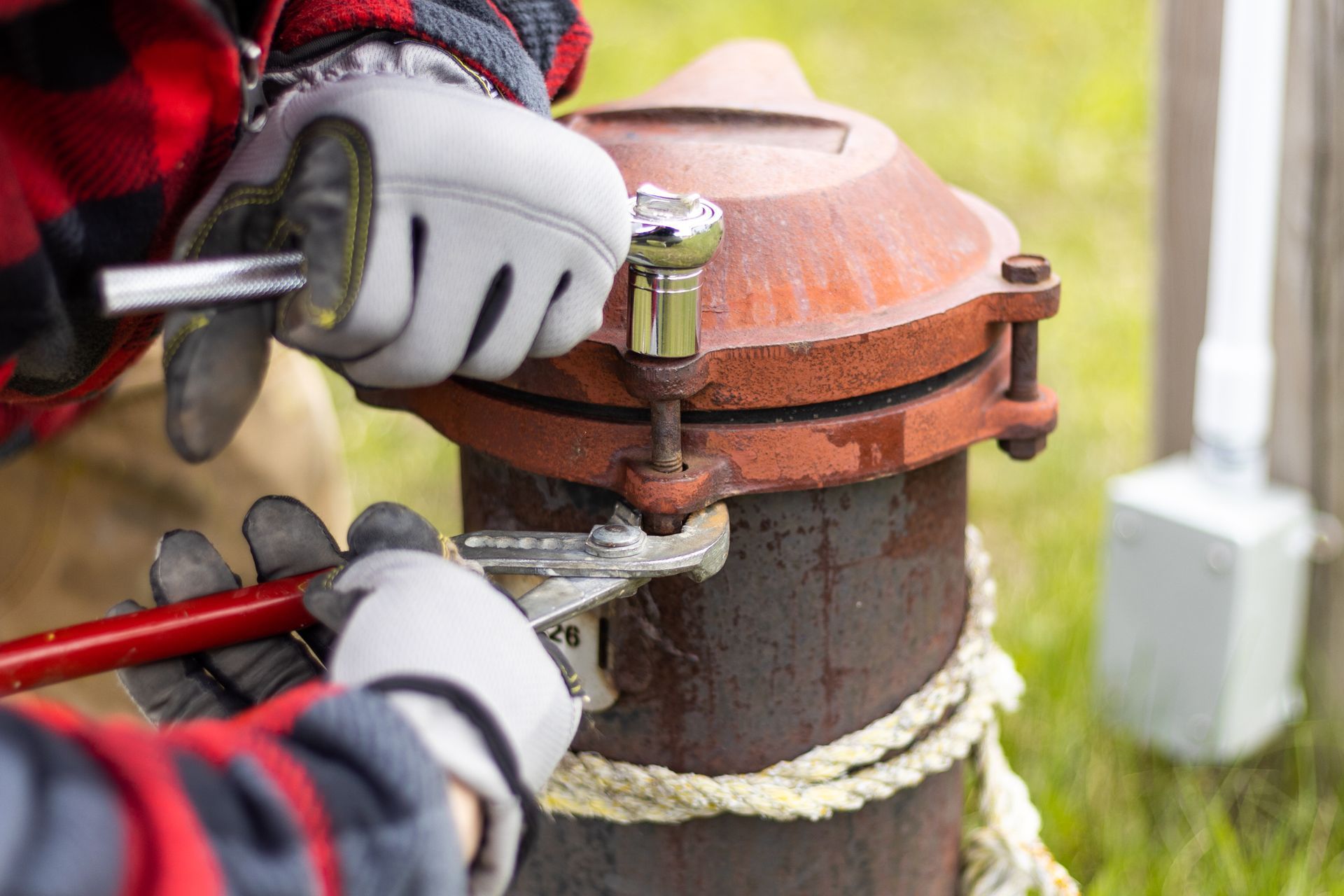 Gloved hands using a wrench to tighten a pipe fitting on a fire hydrant valve