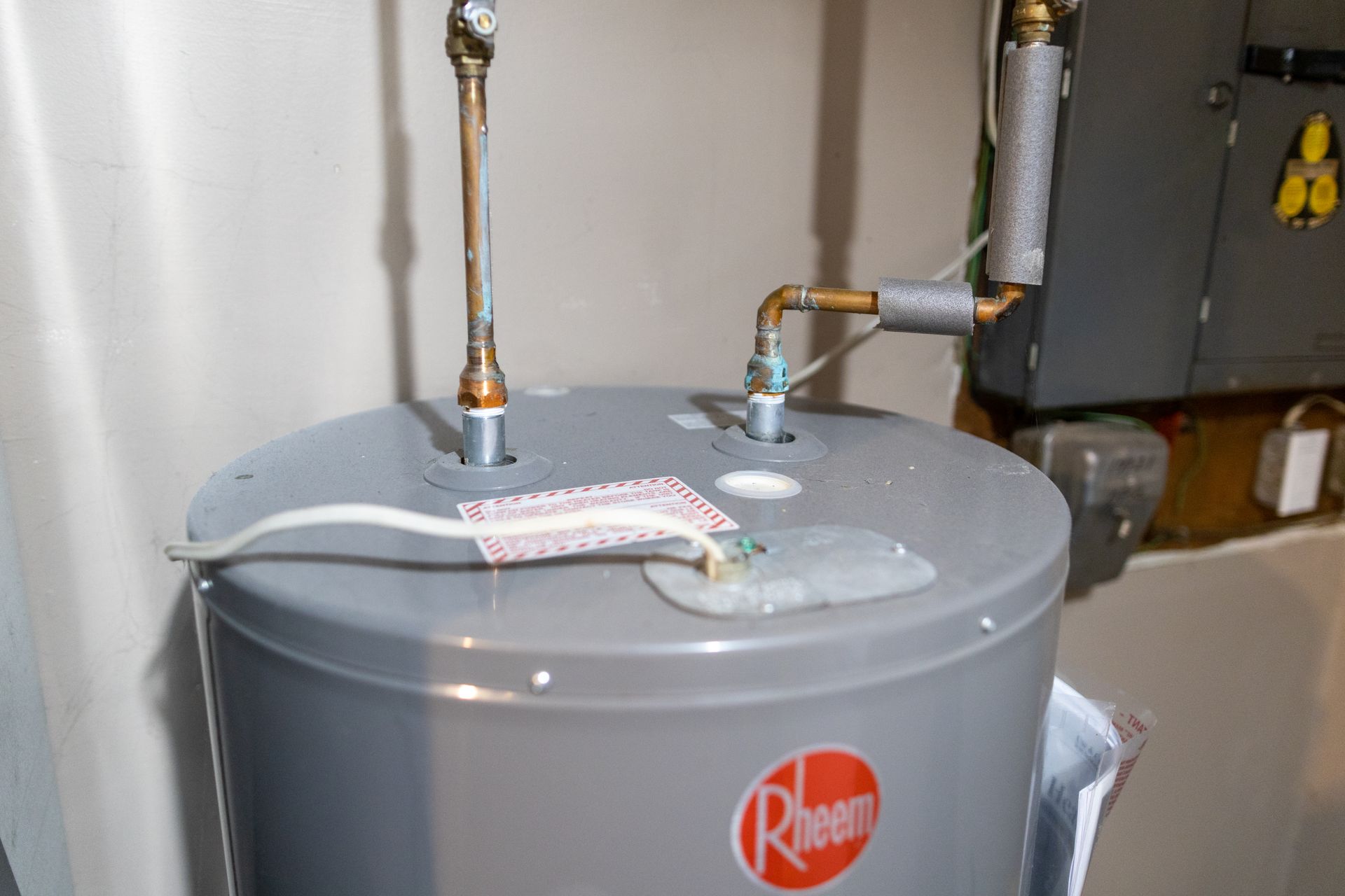 A Rheem water heater with water leaking from the top near pipes and connections.