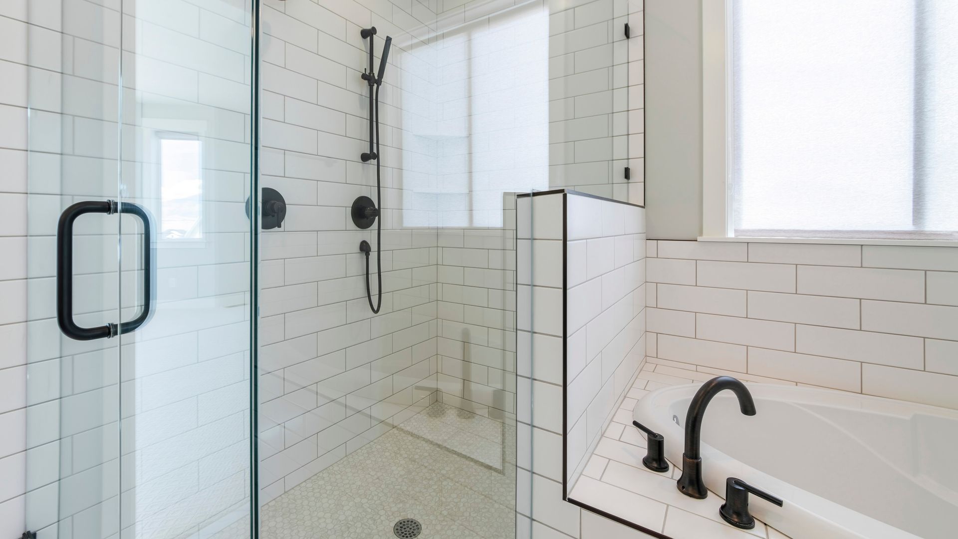 Modern white bathroom with black fixtures: shower, tub, and window.