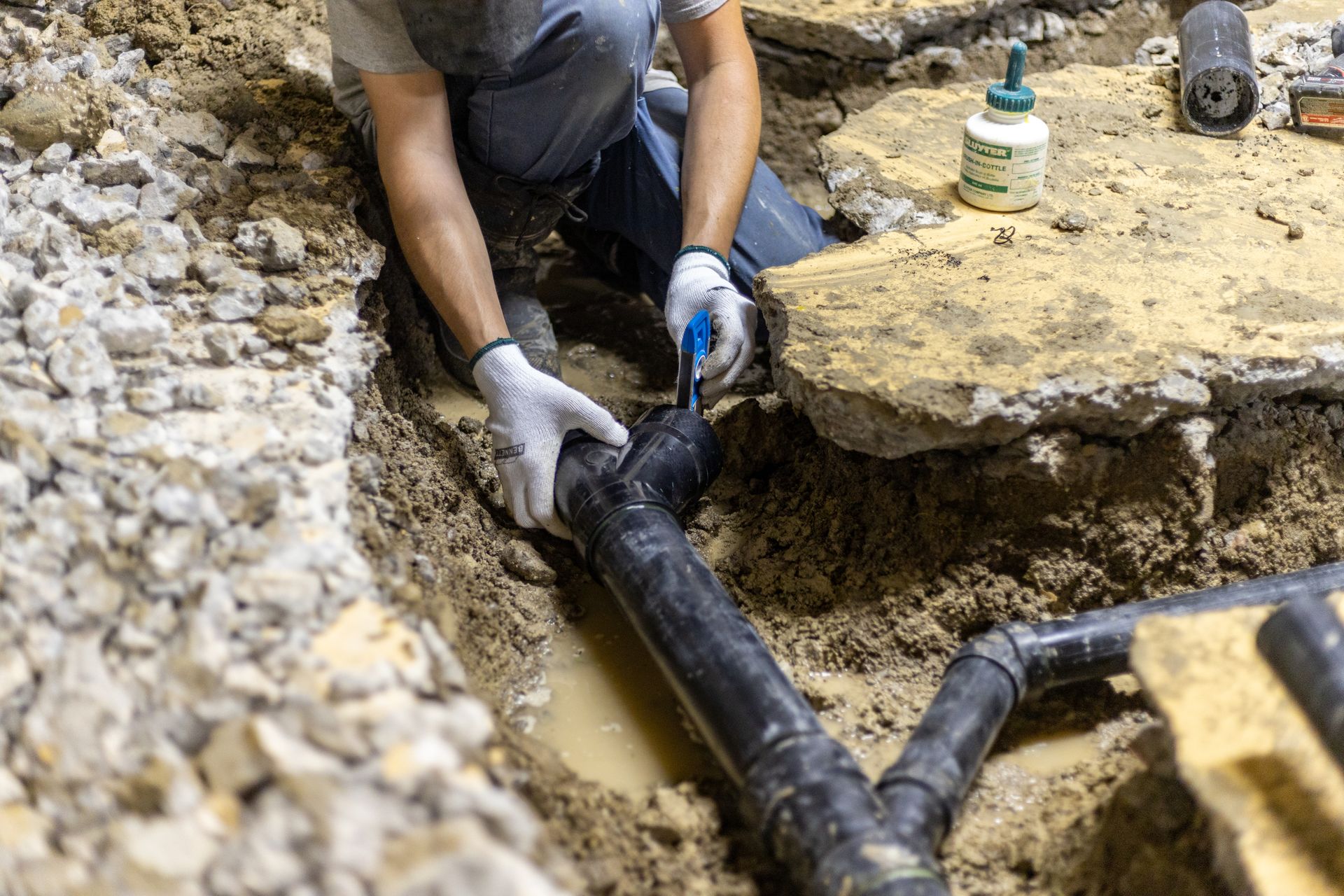 A man is kneeling down in the dirt fixing a pipe.
