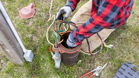 Gloved worker handling colorful cables beside an open utility box outdoors