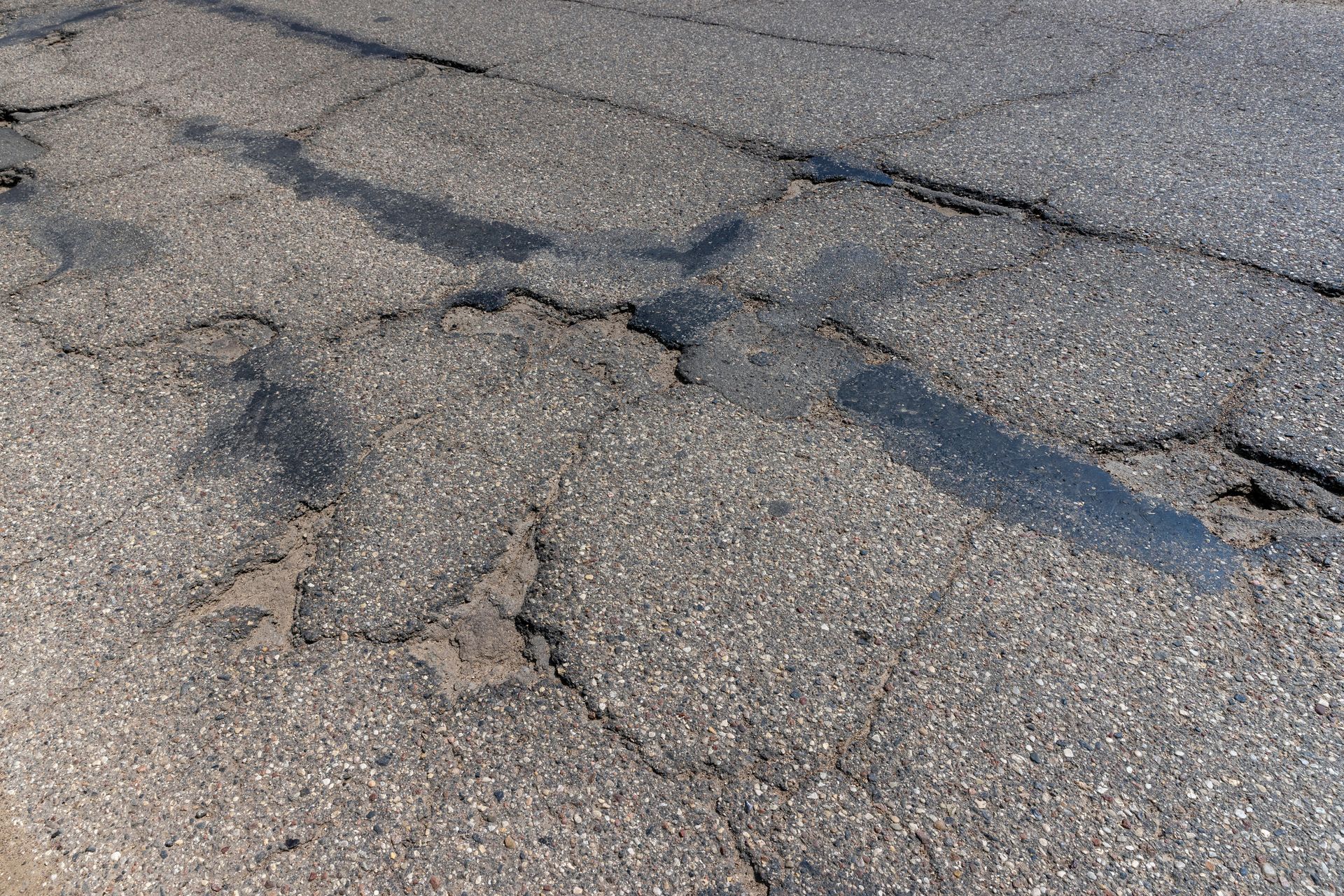 cracked and pothole-damaged asphalt driveway in need of repair or replacement
