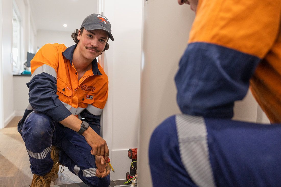 A Man in an Orange Shirt and Blue Pants is Working on a Pipe — Macquarie Electric in Narromine, NSW